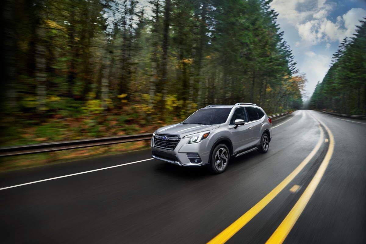 A silver 2023 Subaru Forester driving down a wooded highway.