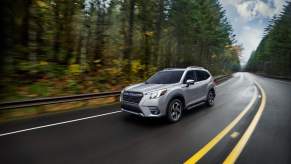 A silver 2023 Subaru Forester driving down a wooded highway.