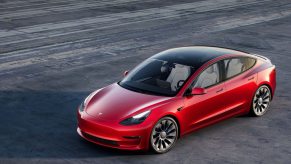 A red Tesla Model 3 parked on pavement.