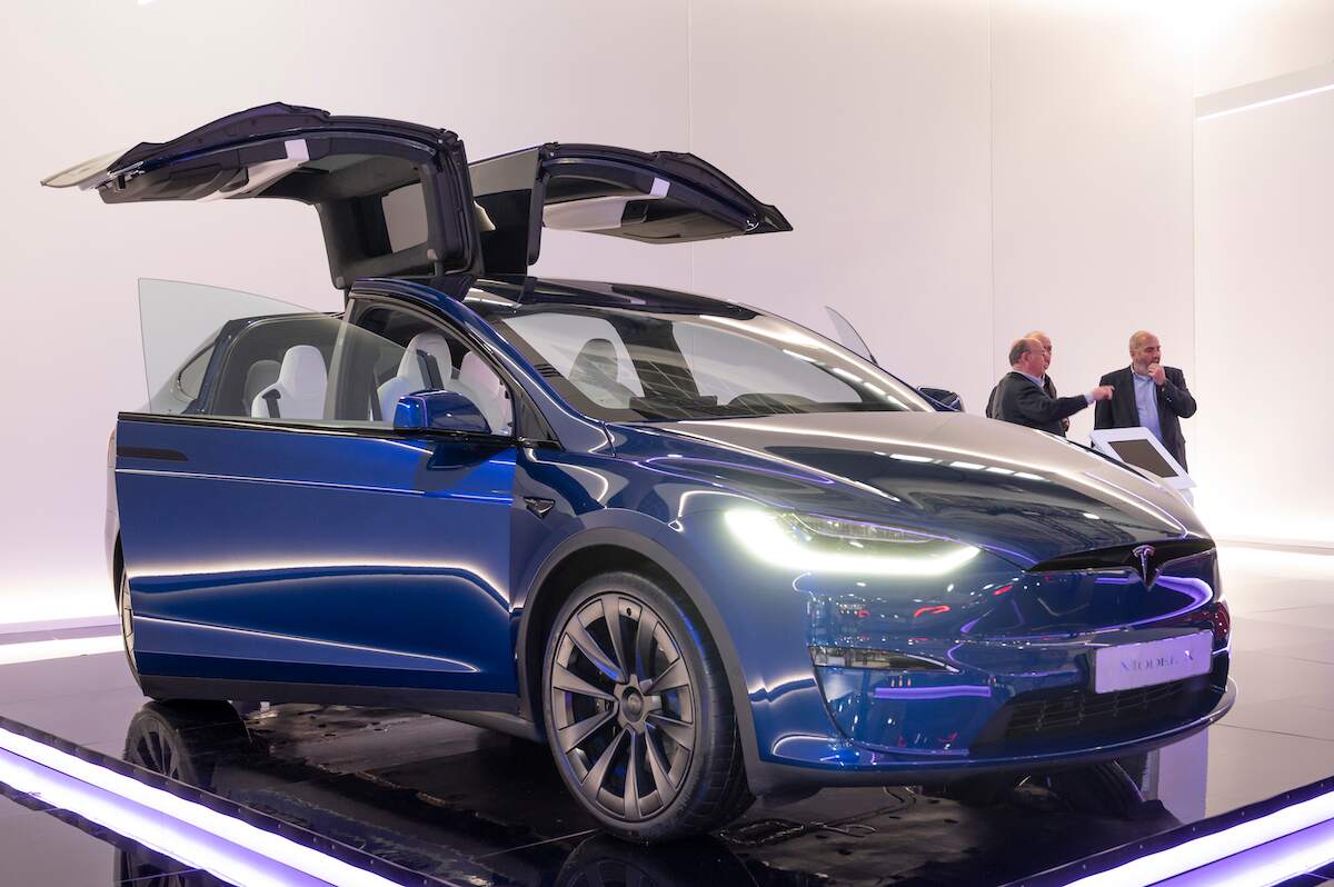 A blue 2023 Tesla Model X parked indoors with the doors up.