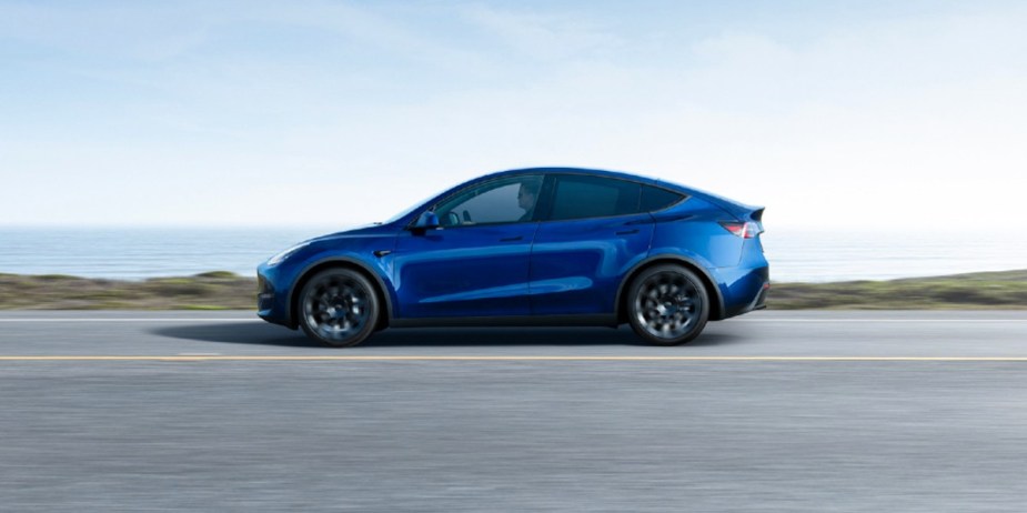 A blue 2023 Tesla Model Y small electric SUV is driving on the road. 