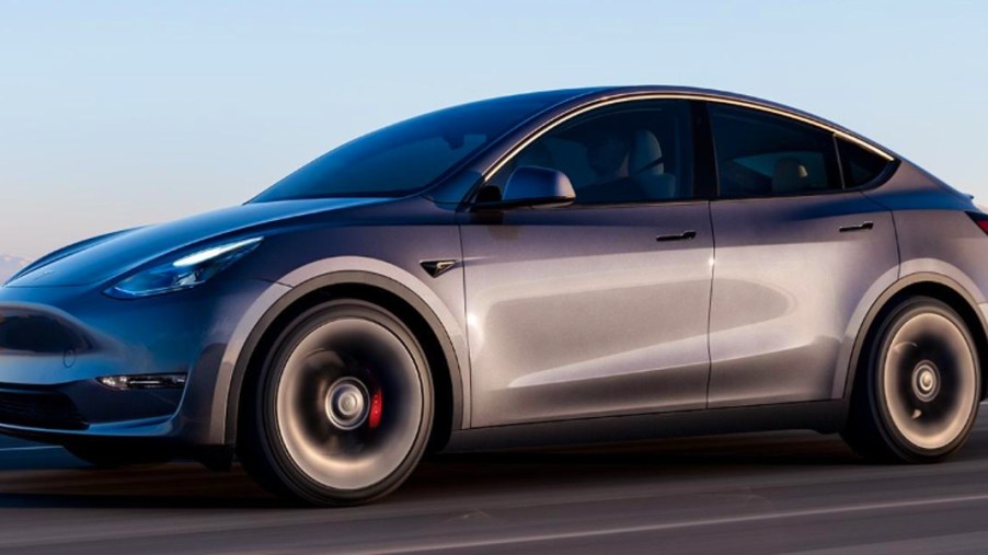 A gray 2023 Tesla Model Y small electric SUV is driving on the road.