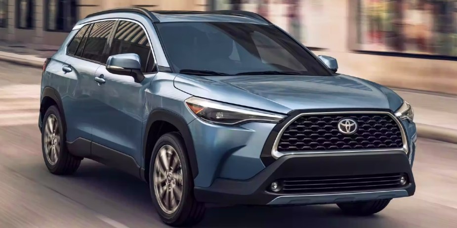 A blue 2023 Toyota Corolla Cross subcompact SUV is driving on the road. 
