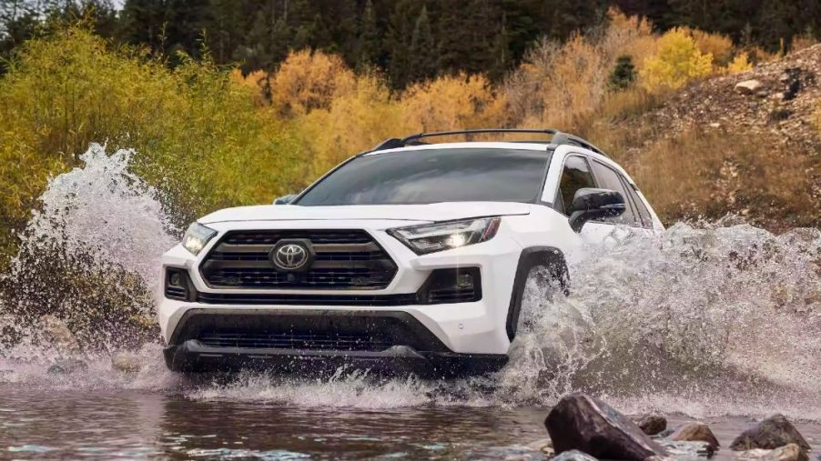 A white 2023 Toyota RAV4 small SUV is driving through water.