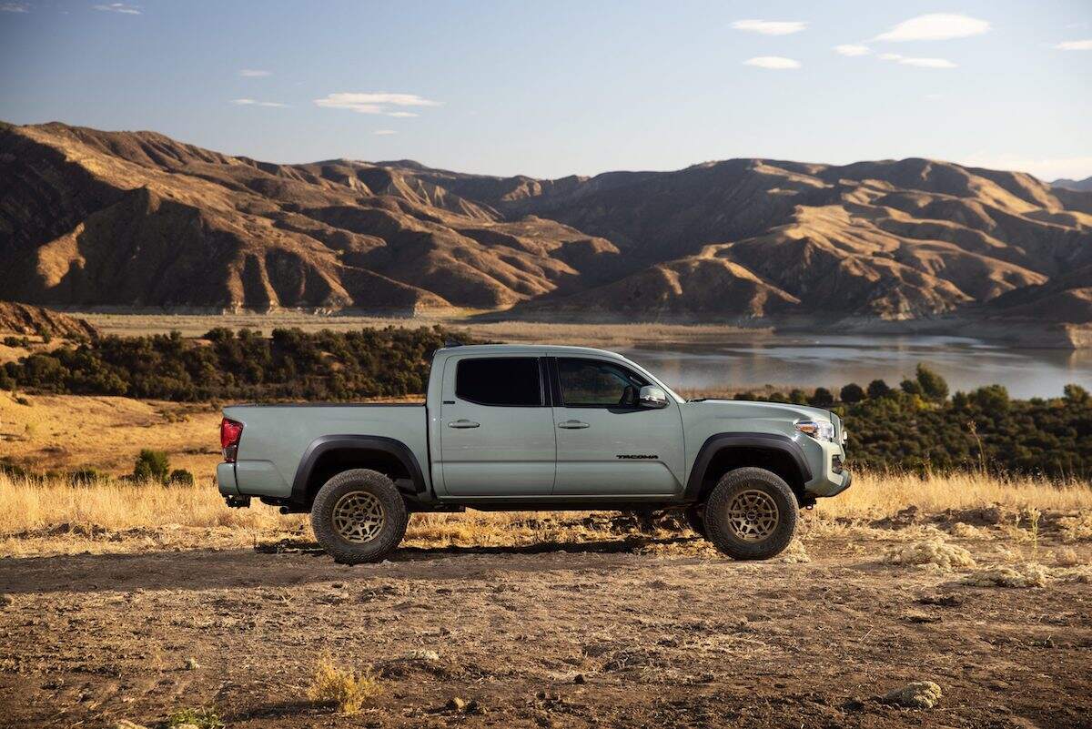 A light color 2023 Toyota Tacoma parked in front of a mountainside with a body of water in a more desert style area.