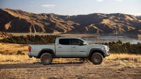A light color 2023 Toyota Tacoma parked in front of a mountainside with a body of water in a more desert style area.