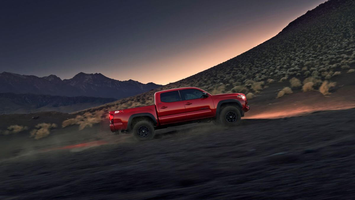 A red 2023 Toyota Tacoma with SX Package midsize pickup truck model climbing up a dirt hill at dusk