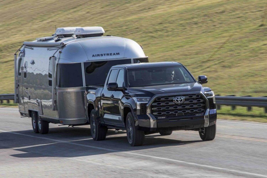 Toyota demonstrates the new V6 Tundra's high towing mileage by pulling an airstream down the road, a grassy field visible in the background.