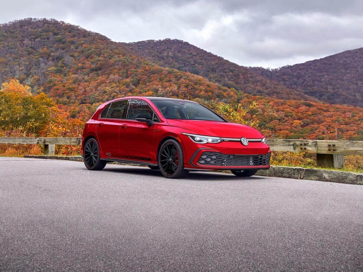 A red 2023 Volkswagen Golf GTI parks next to a hilly landscape.