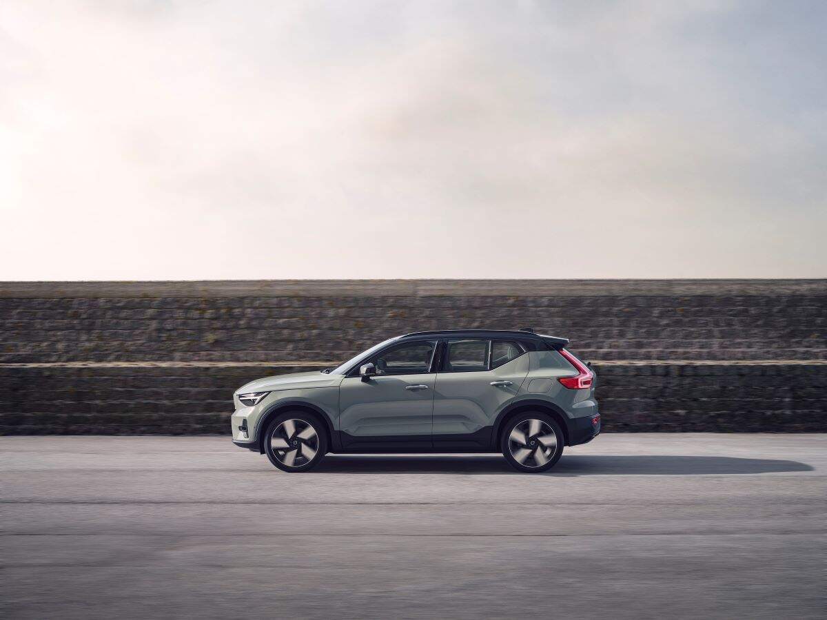 A silver 2023 Volvo C40 Recharge parked in front of a grey stone wall on blacktop.