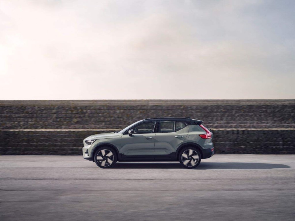 A silver 2023 Volvo XC40 Recharge parked in front of a grey stone wall on blacktop.