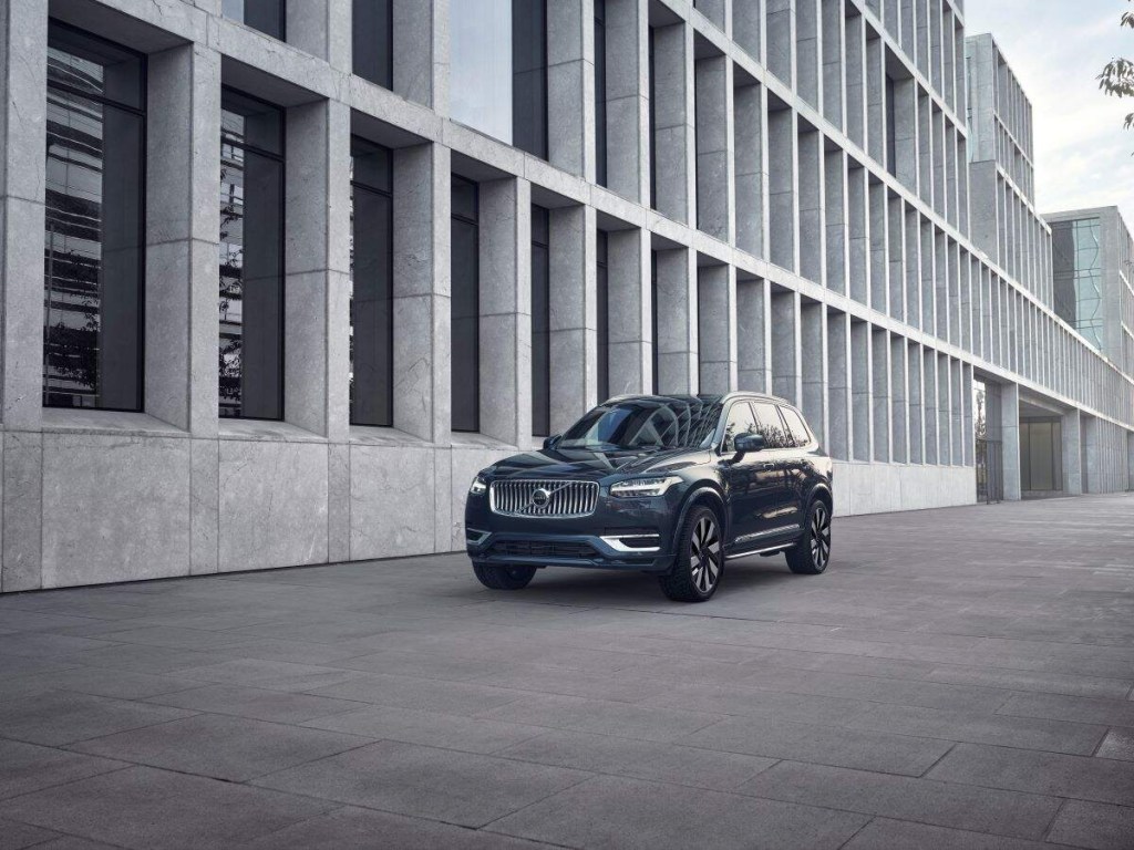 A dark color 2023 Volvo XC90 parked in front of a building lined with concrete framed windows.