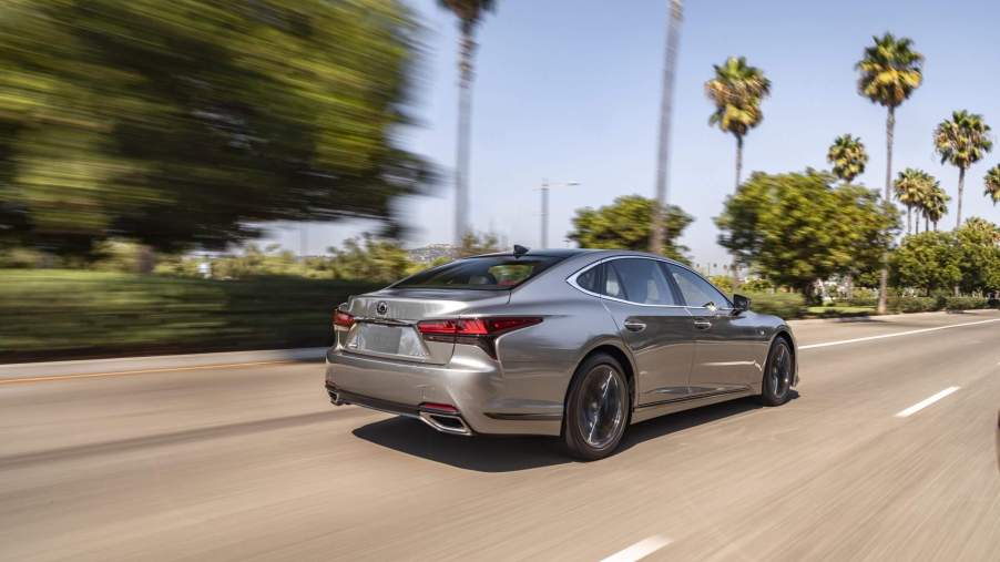 The 2023 Lexus LS speeding down a sunny road with trees.