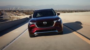 Front view of a new Mazda CX-90 in red driving down a highway with a straight-six engine under the hood.