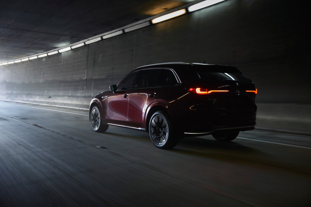 Rear view of a new Mazda CX-90 driving through a tunnel with its tail lamps illuminated. 