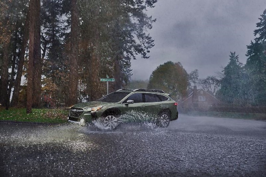 A green 2023 Subaru Outback corners in the wet. 