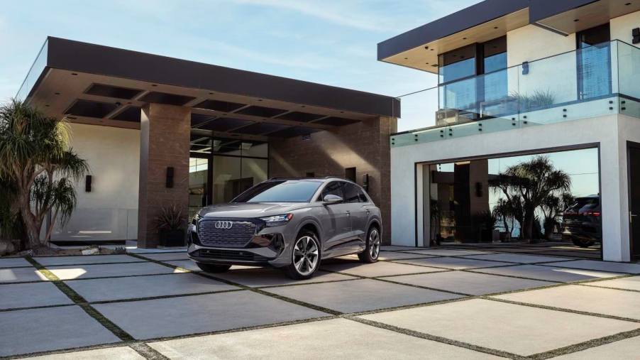 A grey Audi E-Tron electric SUV sits in front of a luxury home.