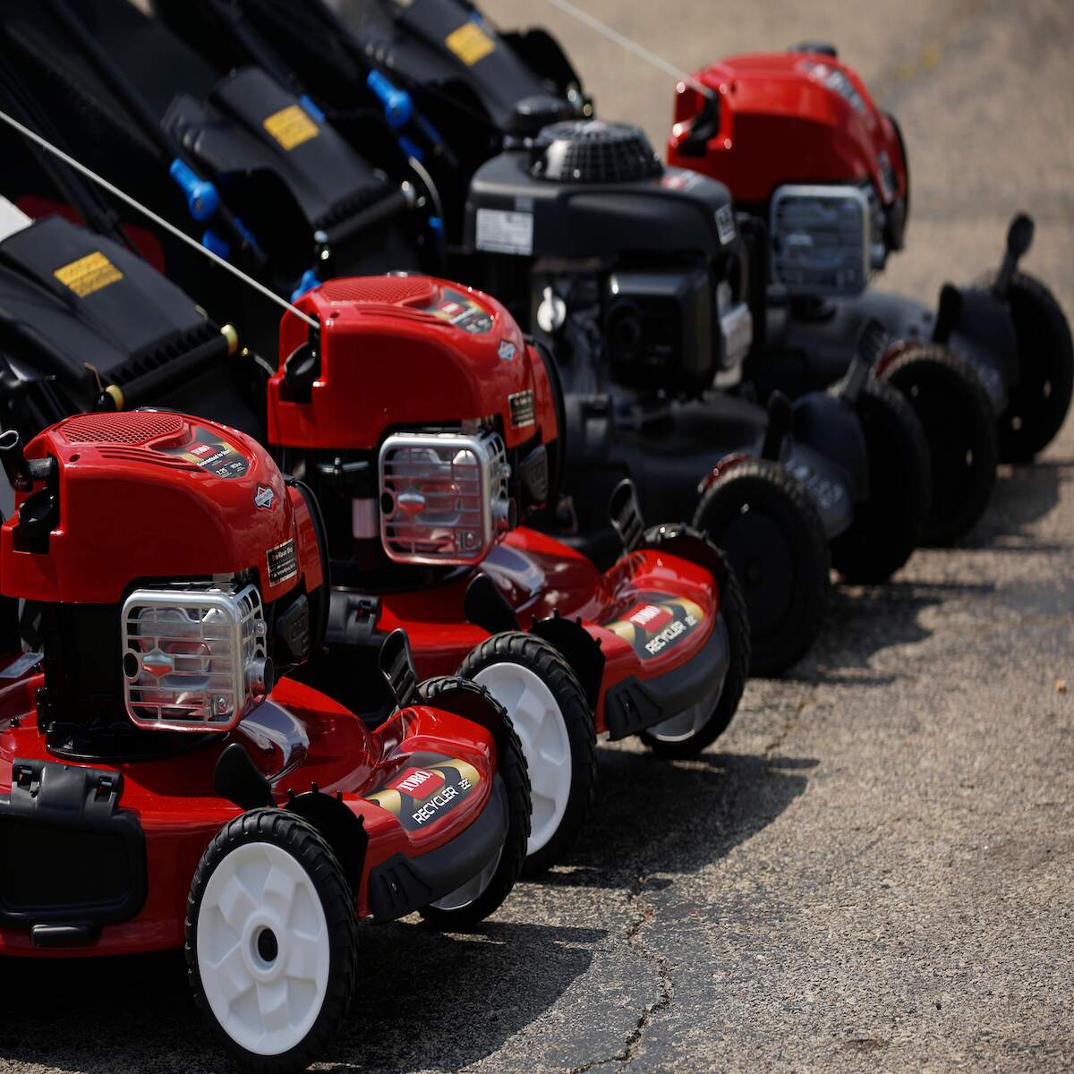 A row of push mowers that might be in the need of having them remove the lawn mower blades for maintenance, all in red.