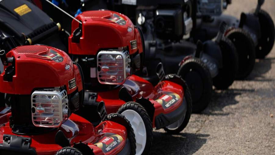 A row of push mowers that might be in the need of having them remove the lawn mower blades for maintenance, all in red.