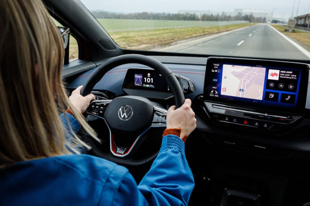 A woman drives her Volkswagen EV down a road.