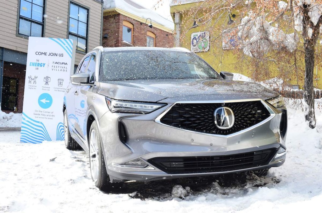 A silver Acura MDX parked outdoors in the snow in front of a building.