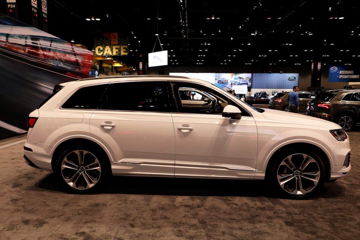 A white Audi Q7 parked indoors with a black background and screens.