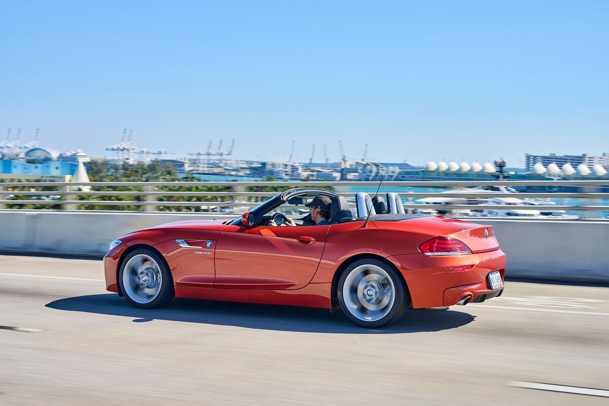 An orange BMW Z4 hard-top convertible shows off its sports car looks by a marina.