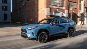 A blue Toyota RAV4 drives on a city street. The RAV4 failed to earn the title of best compact SUV for the money.