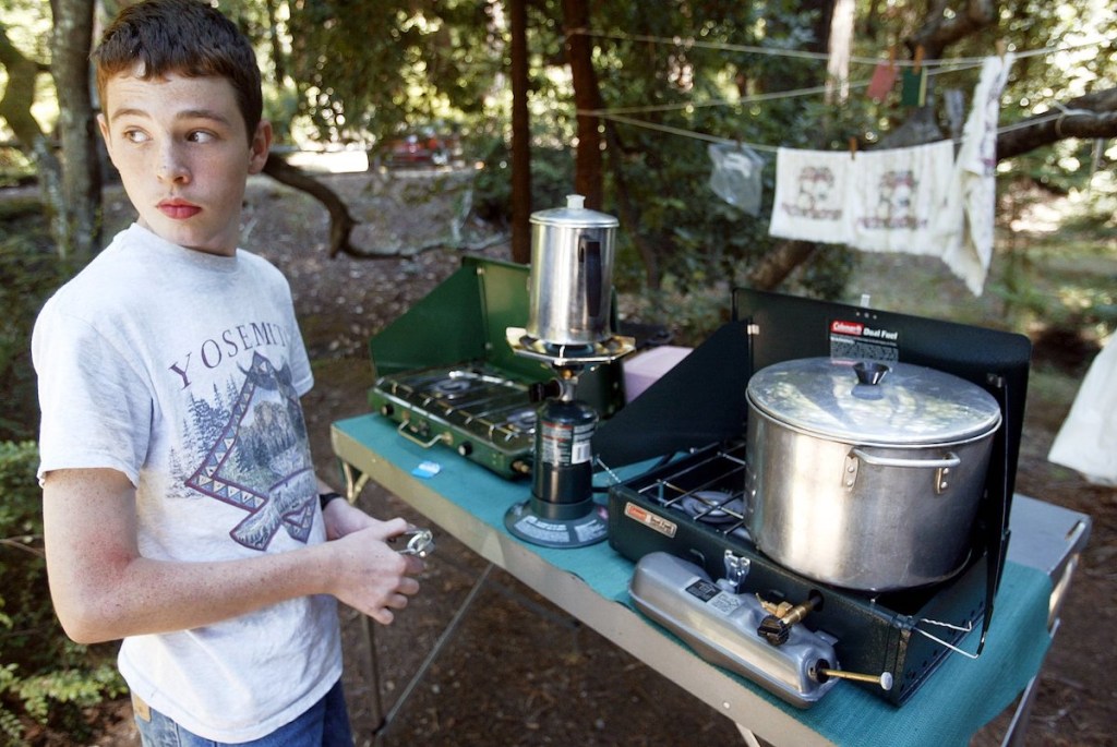 A kid standing next to a set of camping stoves. A great was to camp on a budget. 