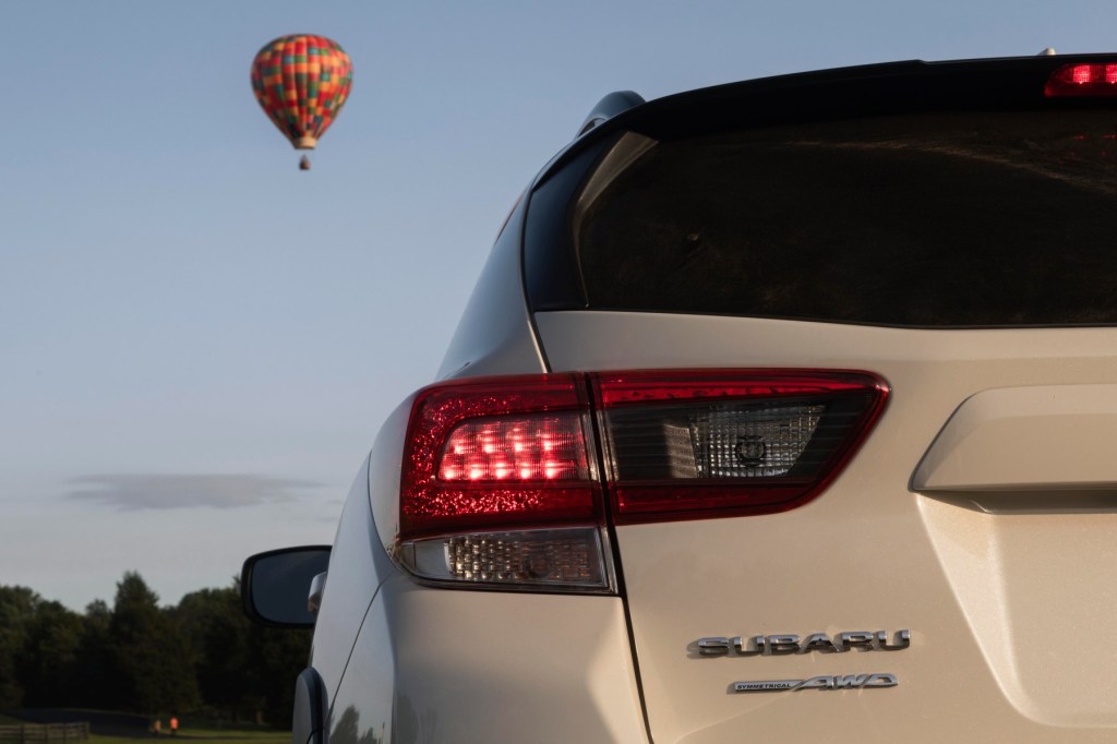 Rear view of a white Subaru Crosstrek, the cheapest Subaru SUV, with a hot air balloon floating in the background. 