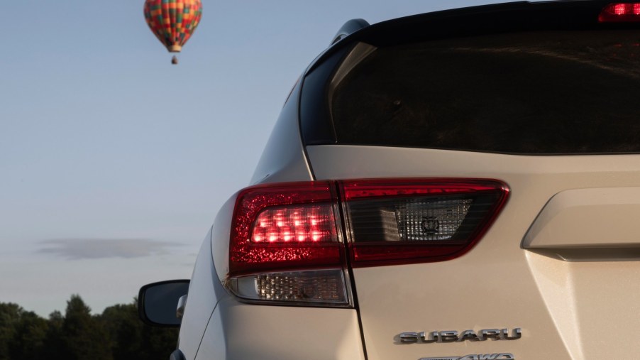 Rear view of a white Subaru Crosstrek, the cheapest Subaru SUV, with a hot air balloon floating in the background.
