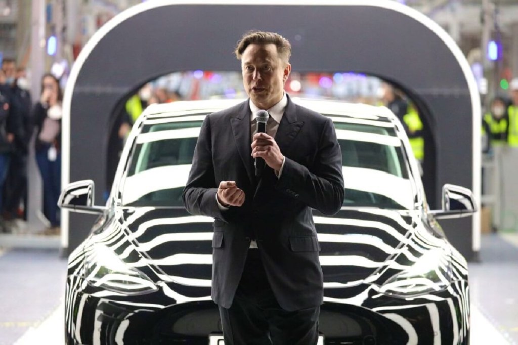 Elon Musk gives a speech next to a Tesla EV. 