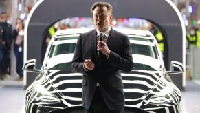 Elon Musk gives a speech next to a Tesla EV.