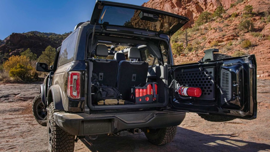 The rear end of a Ford Bronco with its hatch opened to display off-road gear. A rocky desert landscape surrounds. 