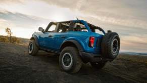 A blue 2023 Ford Bronco climbs a hill off-road with its top down. The Bronco still hans't beat the Jeep Wrangler in sales.