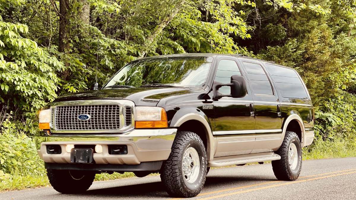A Ford Excursion parked next to a forest