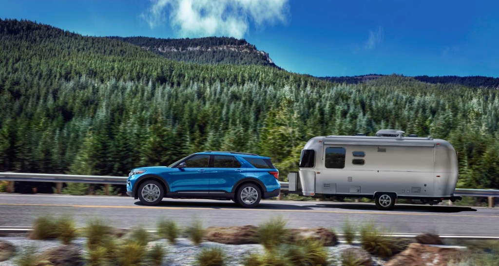 Blue Ford Explorer tows a camper along a mountain road. 