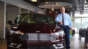 The Manderbach Ford general sales manager posing with a dark red Ford Fusion Energi hybrid midsize sedan model