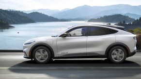 A white 2023 Ford Mustang Mach-E small electric SUV is driving on the road.