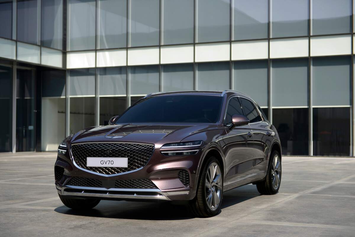 A black Genesis GV70, a compact luxury SUV that could be best for you, parked in front of a building with many windows.