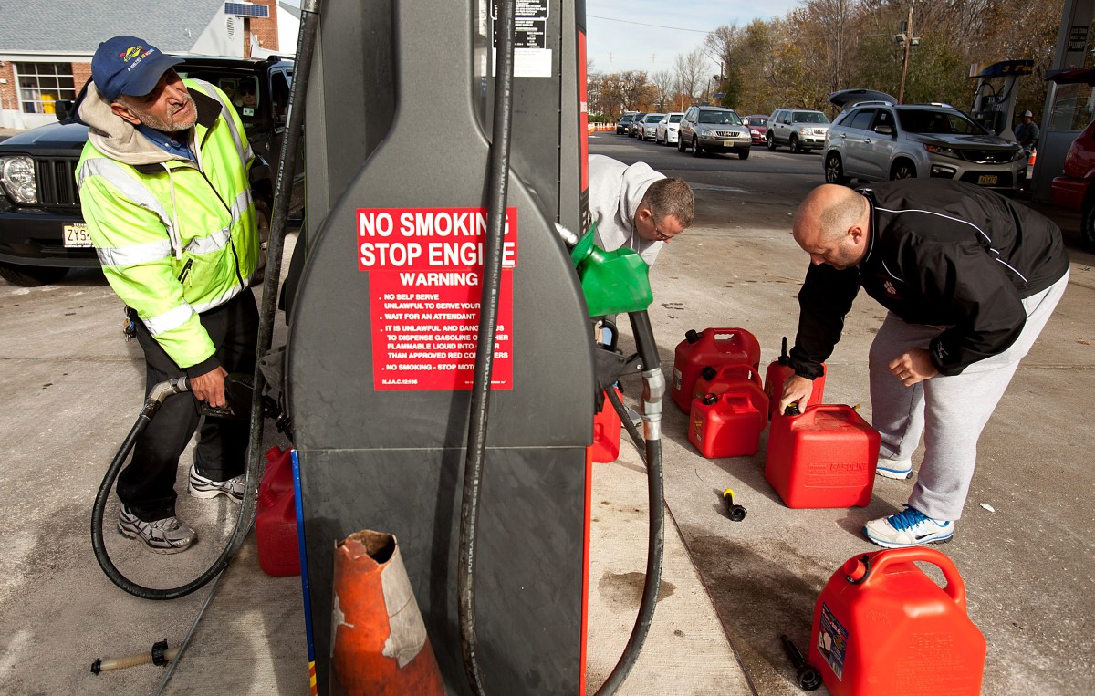 A man fills red gas cans at a gas station