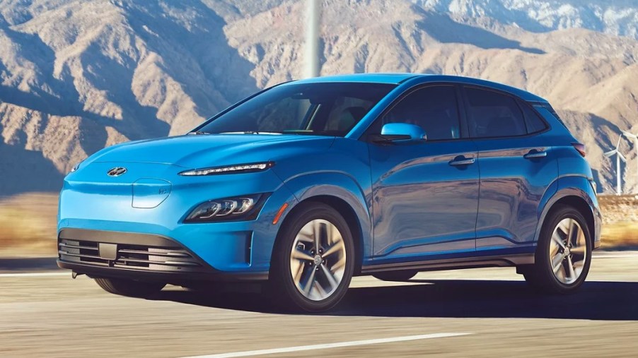 A blue 2023 Hyundai Kona Electric subcompact electric SUV is driving on the road.