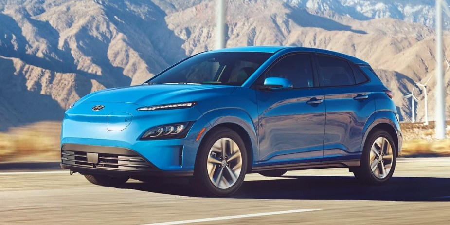 A blue 2023 Hyundai Kona Electric subcompact electric SUV is driving on the road. 