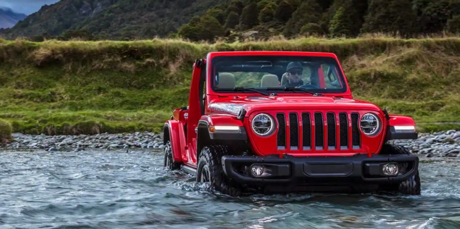 A red 2023 Jeep Wrangler small off-road SUV is wading through water. 