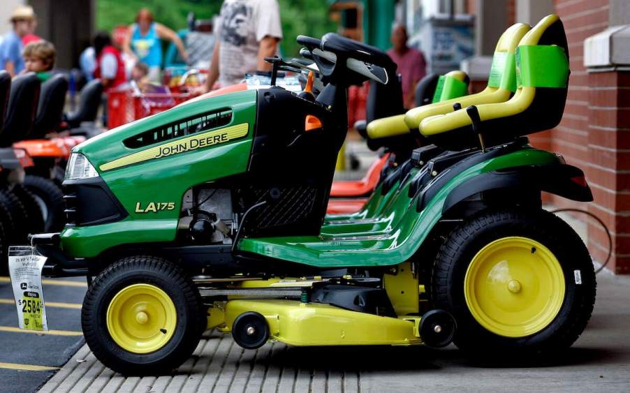 A green John Deere lawn mower parked outdoors that the owner may need to know how to charge a riding lawn mower battery during ownership.