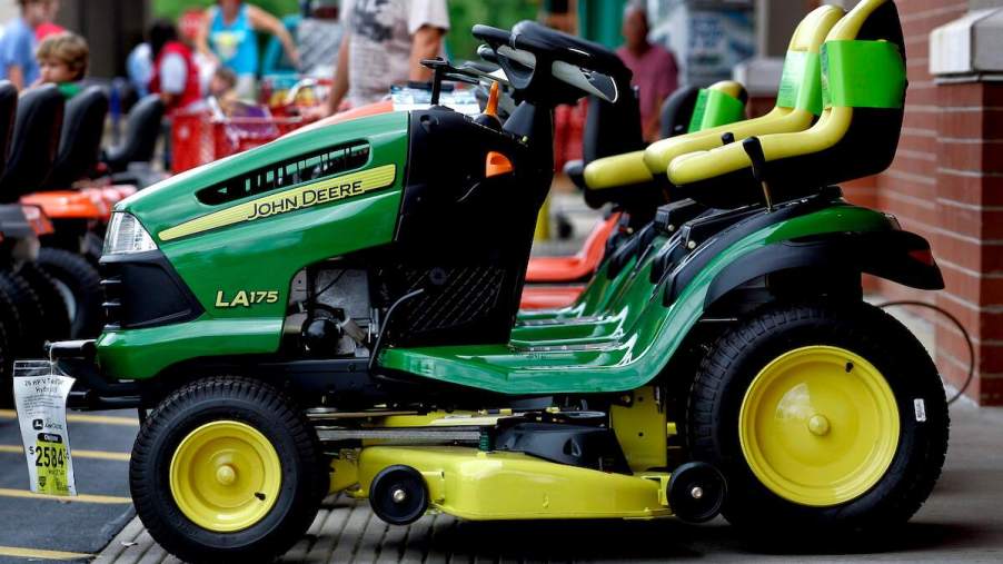 A green John Deere lawn mower parked outdoors that the owner may need to know how to charge a riding lawn mower battery during ownership.