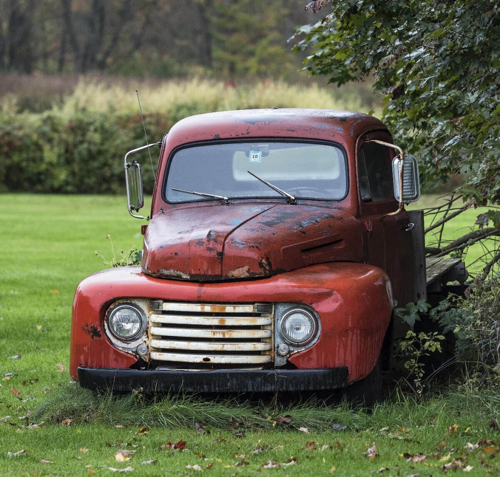 An old truck is parked at a junkyard.