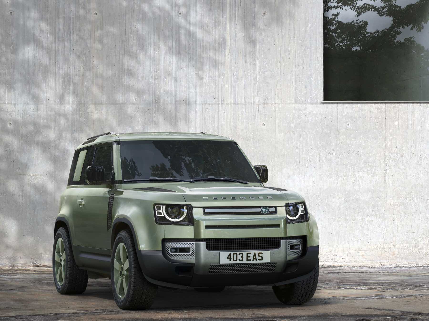 A green Land Rover Defender sits in front of a gray wall. The Defender is a top competitor against the Mercedes-Benz G Class.