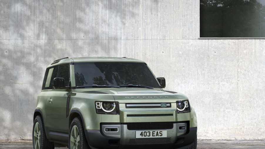 A green Land Rover Defender sits in front of a gray wall. The Defender is a top competitor against the Mercedes-Benz G Class.