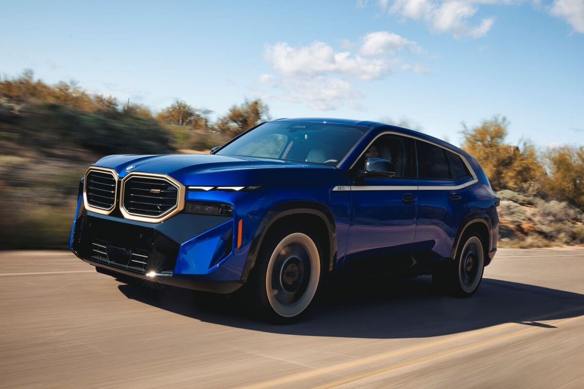 A Marina Bay Blue 2023 BMW XM full-size luxury SUV model driving down a country highway
